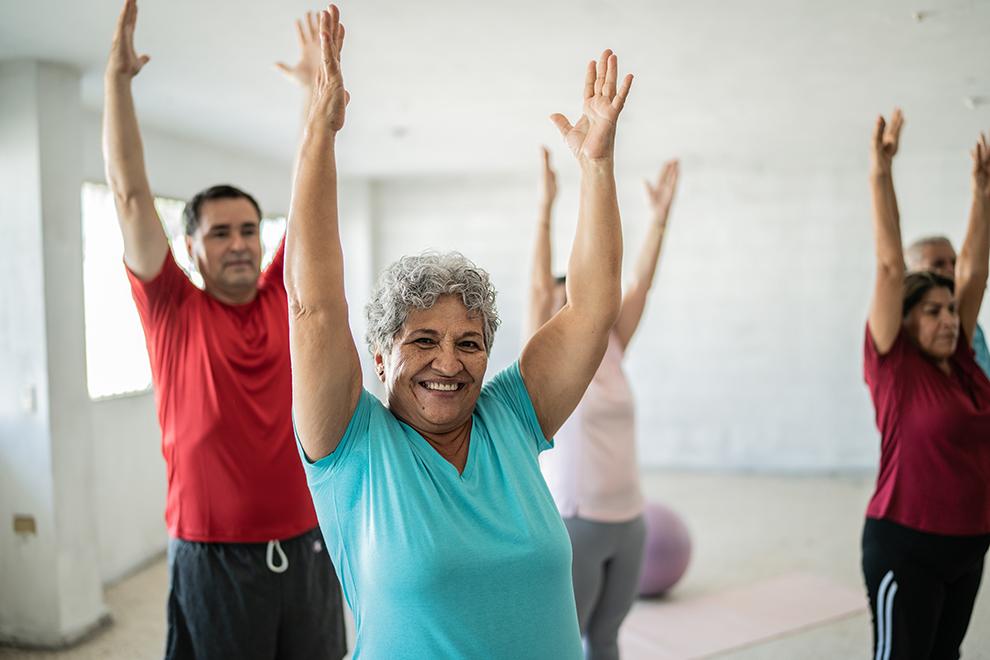 a group of people in an exercise class stretching with arms straight in the air